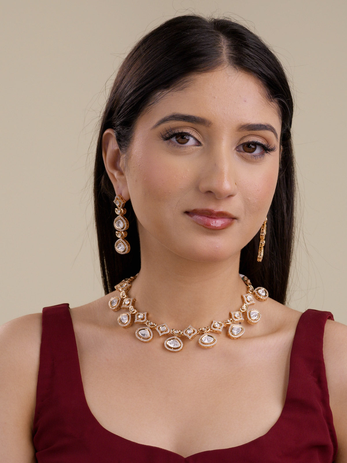 Front model view wearing a Kundan necklace set in champagne gold tone, showing teardrop kundan-look stones, angled stone stations, American Diamond detailing, curved link accents, and matching drop earrings.