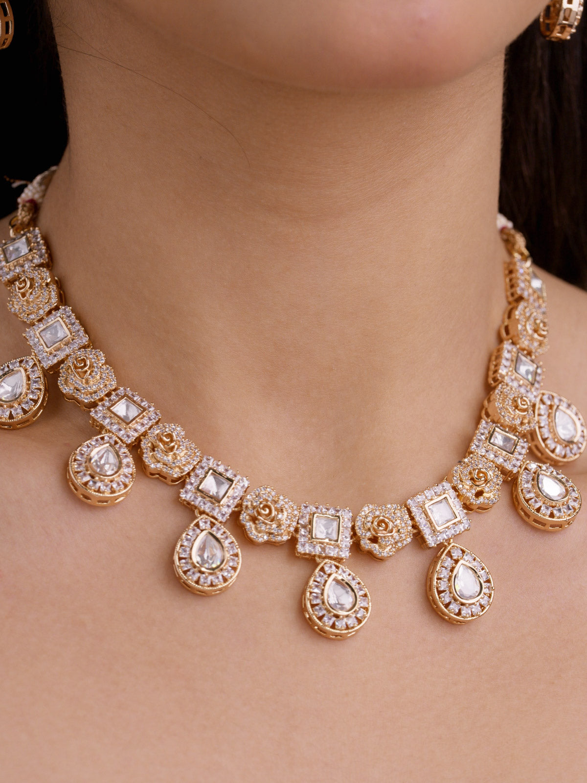 Close-up of a Kundan necklace set in champagne gold tone, showing rose-shaped motifs, square kundan-look stone panels, pear-shaped drops, and American Diamond detailing.