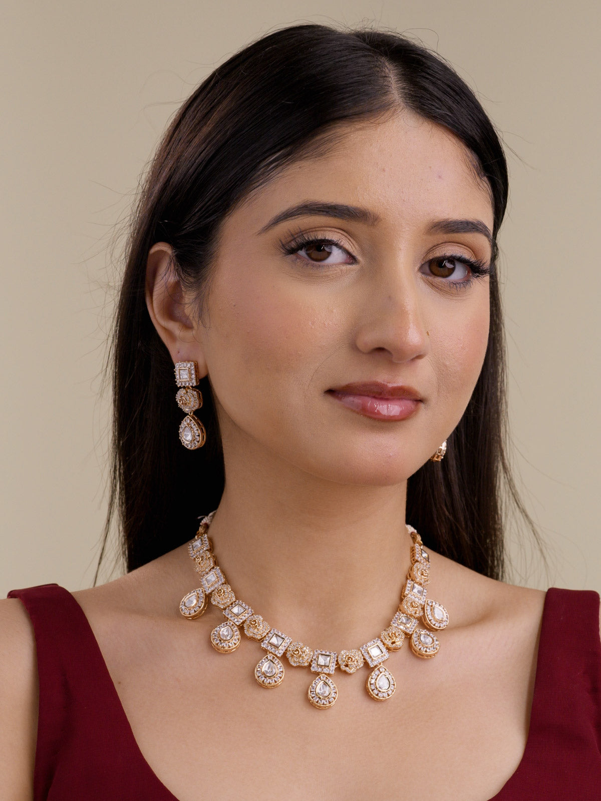 Model wearing a Kundan necklace set in champagne gold tone with matching earrings, showing rose-shaped motifs, square kundan-look stone panels, teardrop drops, and American Diamond detailing.