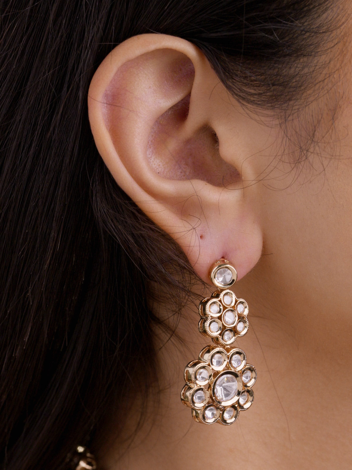 Close-up of model’s ear wearing a champagne gold tone Kundan drop earring with two round floral kundan-look stone clusters.
