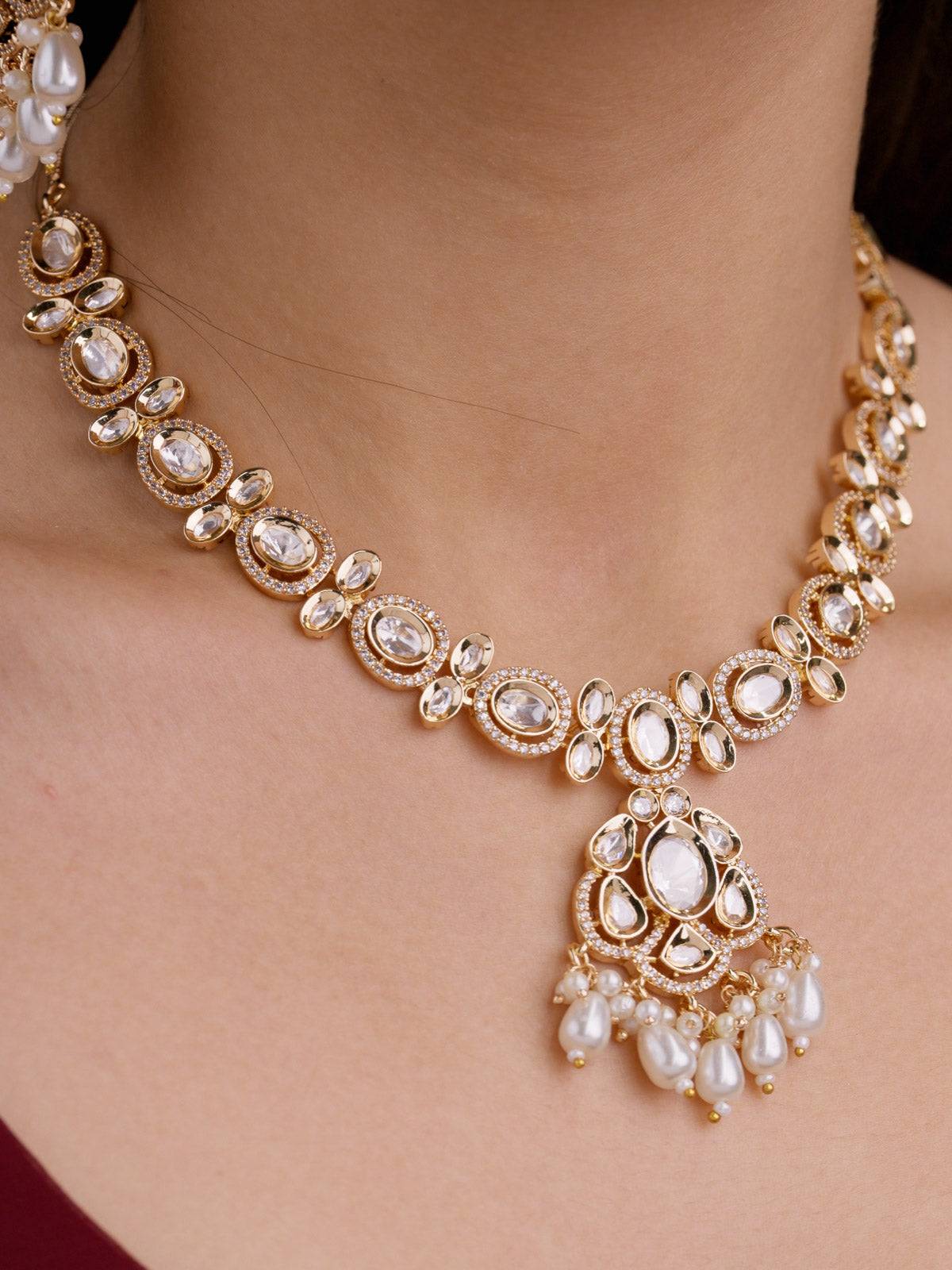 Close-up of champagne gold tone Kundan necklace set with oval kundan-look stones, American Diamond-style borders, centre pendant, pearl-style drops.