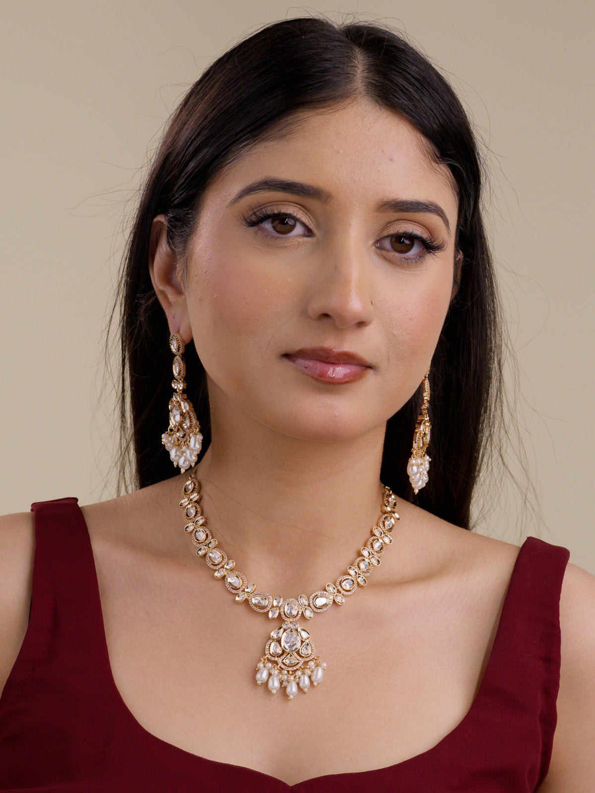 Model wearing champagne gold tone Kundan necklace set with oval kundan-look stones, American Diamond-style borders, centre pendant, pearl-style drops, and matching long earrings.
