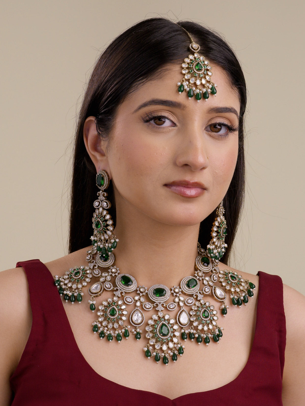Model wearing green bridal Kundan necklace set in antique gold tone with matching earrings and maang tikka, showing green centre stones, teardrop kundan-look stones, American Diamond detailing, and green bead drops.