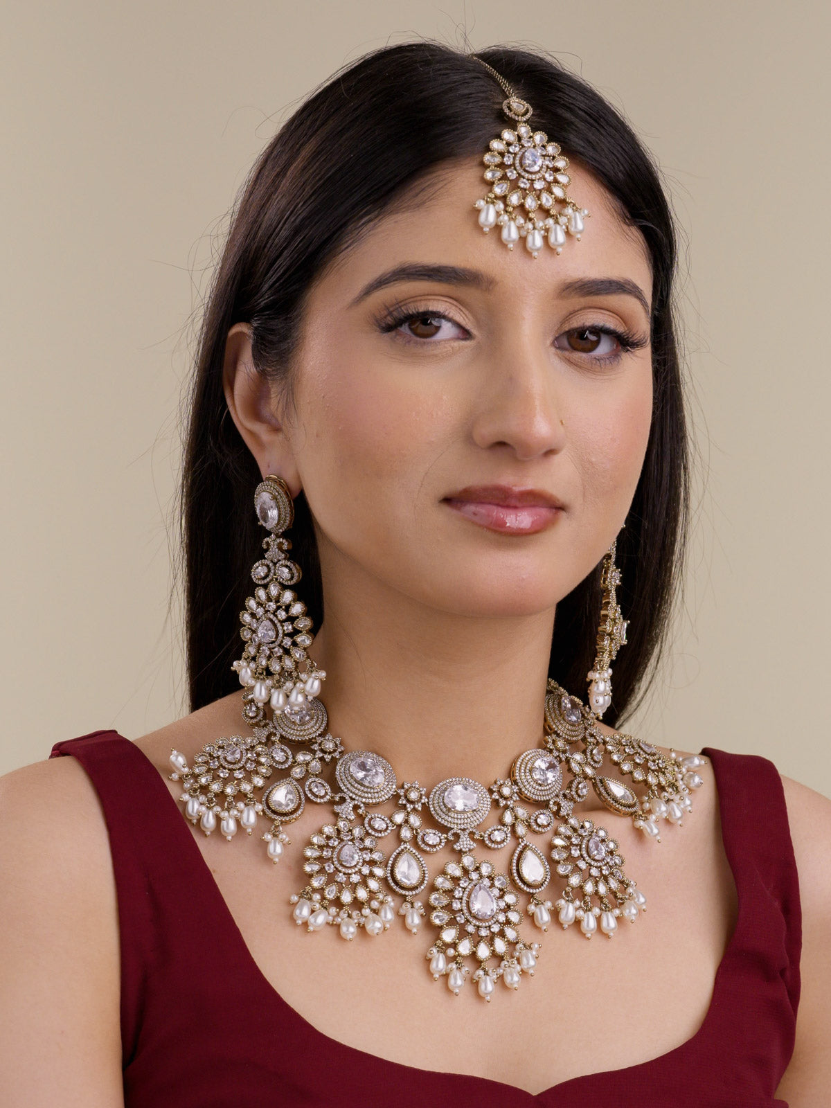 Model wearing neutral Bridal Kundan necklace set in antique gold tone with matching earrings and maang tikka, showing round and teardrop kundan-look stones, American Diamond detailing, and pearl-style drops.