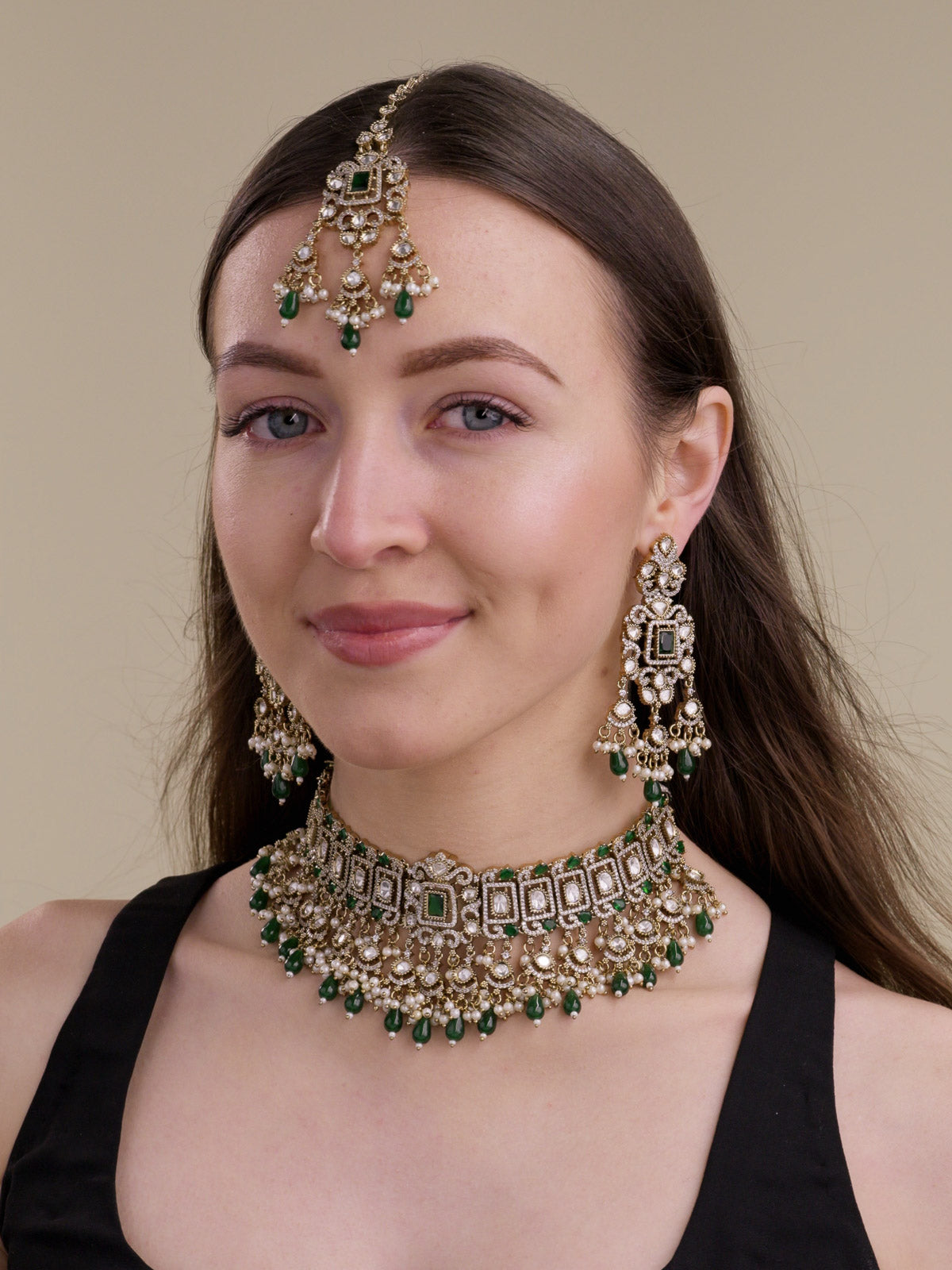 Three-quarter front view of a model wearing a Green Kundan choker-style necklace set in Antique Gold Tone with matching long earrings, maang tikka, rectangular frame detailing, kundan-look centre stones, American Diamond accents, Green drops, and pearl accents.