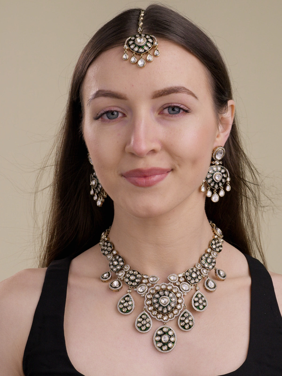 Model wearing an antique gold tone Kundan necklace set with green enamel-look detailing, kundan-look stones, CZ accents, matching earrings, and maang tikka.