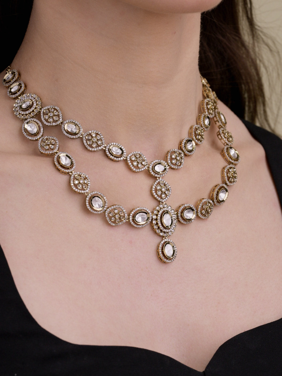 Close-up of a model wearing a multilayer Kundan necklace in Antique Gold Tone with neutral kundan-look stones, AD detailing, oval centre drop and black outfit.