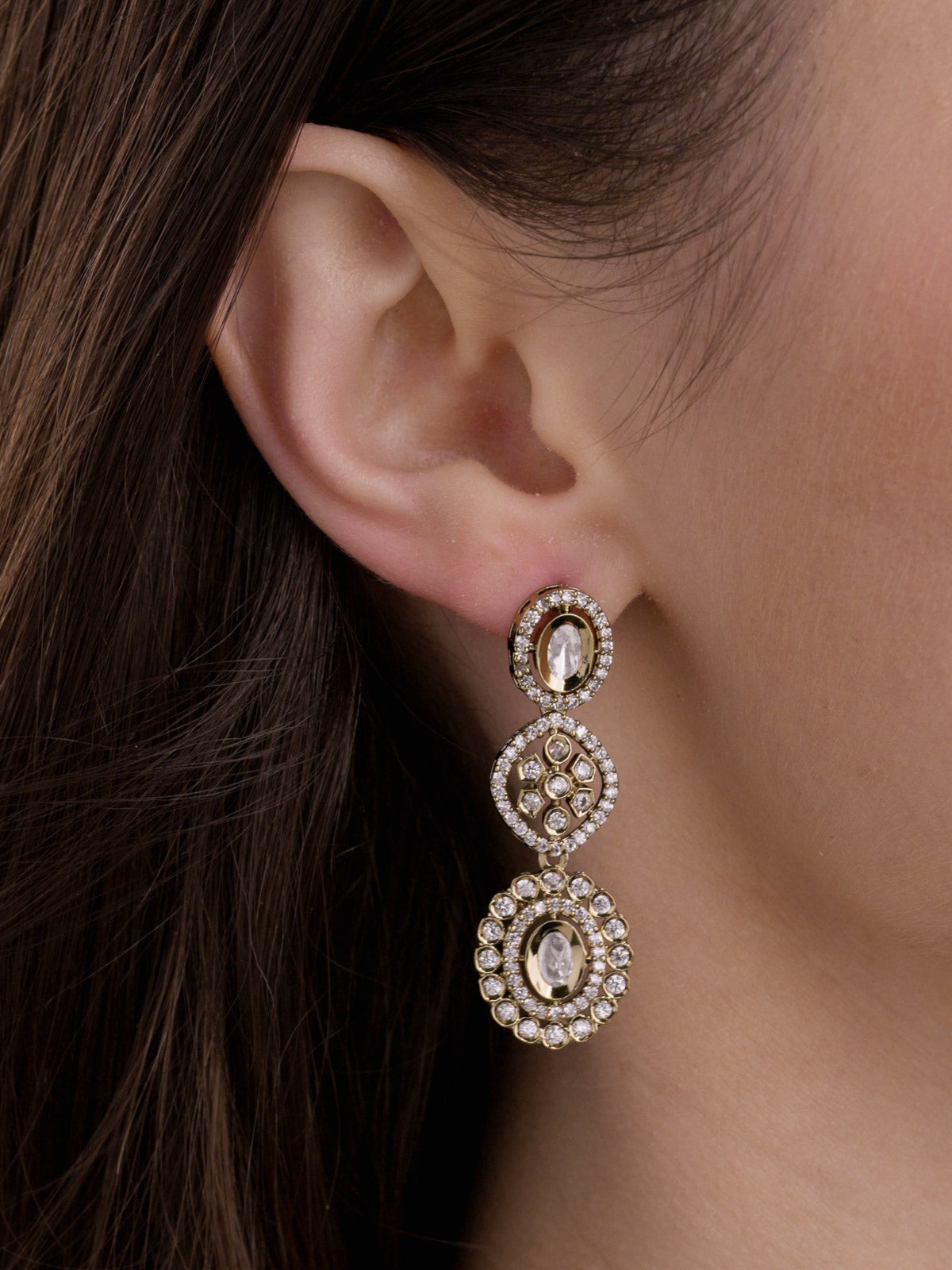 Close-up of a model wearing matching Kundan earrings in Antique Gold Tone with neutral kundan-look stones, oval drops and AD detailing.