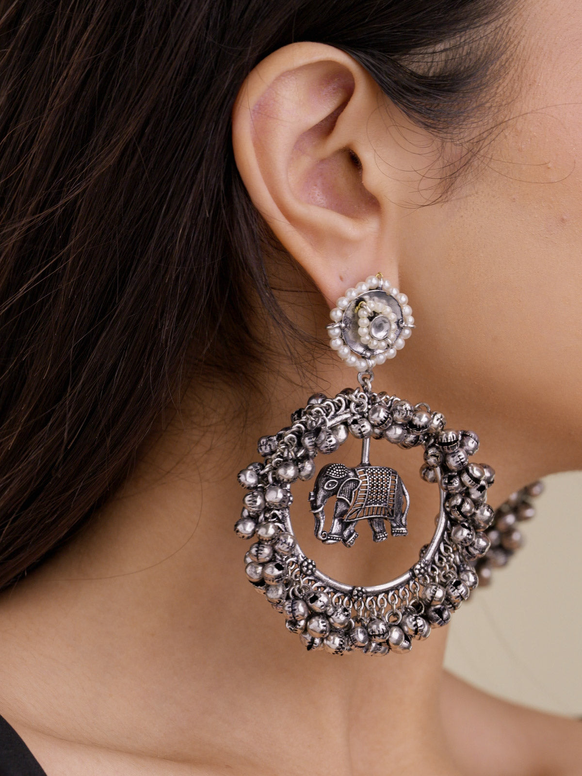 Close-up of model wearing oxidised elephant hoop earrings with pearl-style circular stud tops, suspended elephant motif, and clustered metal bead edging.