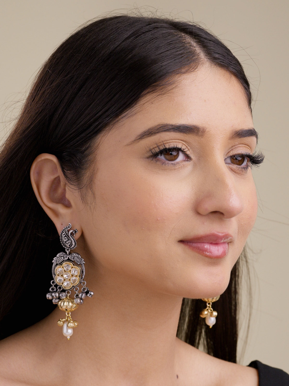 Model wearing oxidised Multi Tone earrings with a peacock-inspired paisley stud motif, round gold-tone kundan-look stone centre, silver bead drops, gold-tone bell detail, and pearl-look lower drop.
