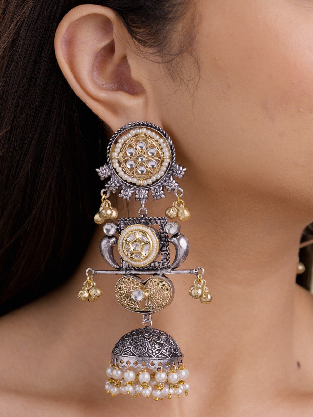 Close-up of a model wearing a statement oxidised multi tone earring with a round kundan-look top, gold-tone bell drops, jhumka dome, and pearl-style lower drops.