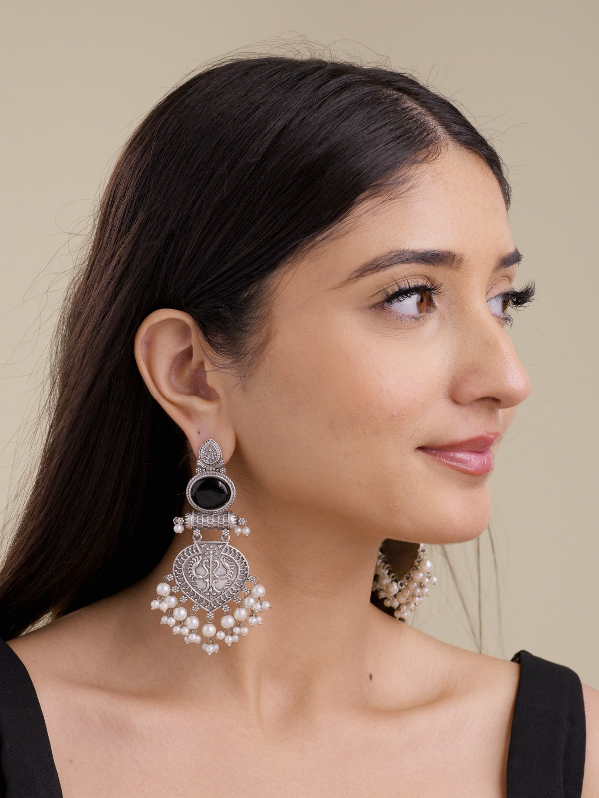 Model wearing statement oxidised earrings with upper black oval stones, carved paan-leaf lower medallions, pearl-style hanging drops, and oxidised silver-tone detailing.