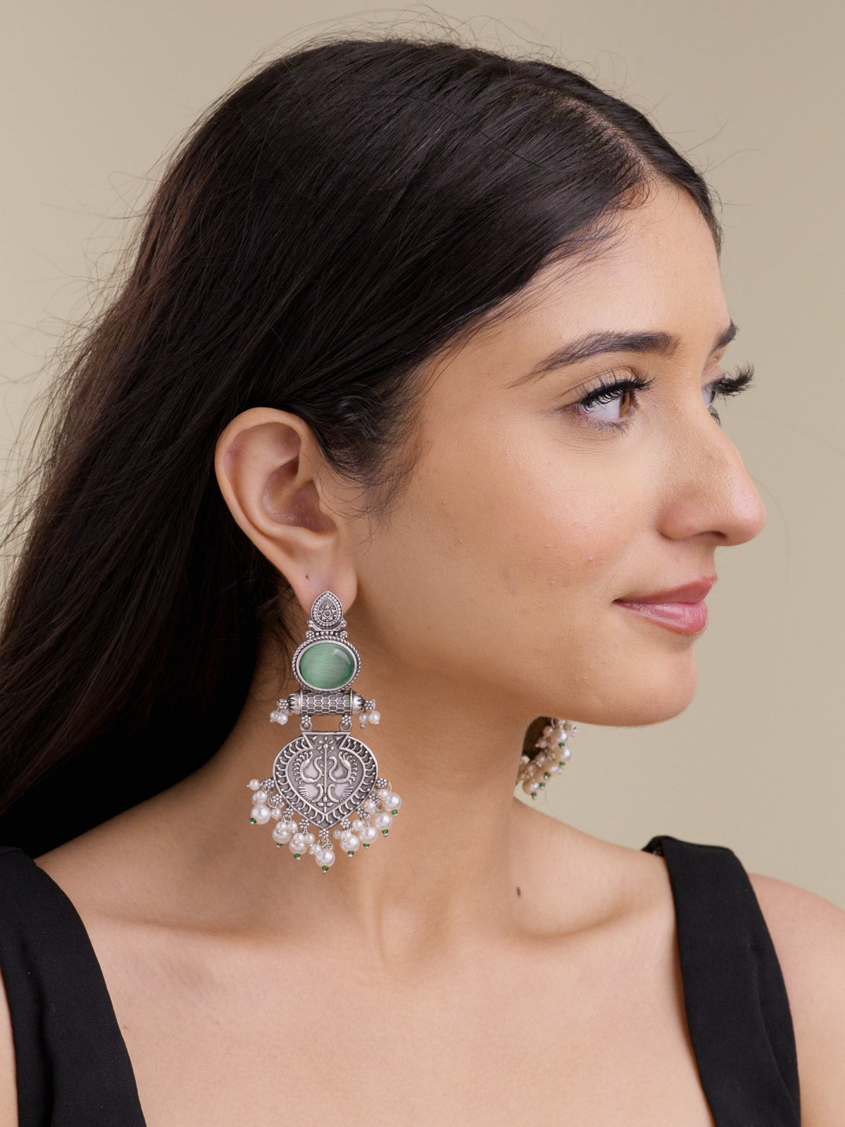 Model wearing statement oxidised earrings with upper mint oval stones, carved paan-leaf lower medallions, pearl-style hanging drops, and small green bead accents.