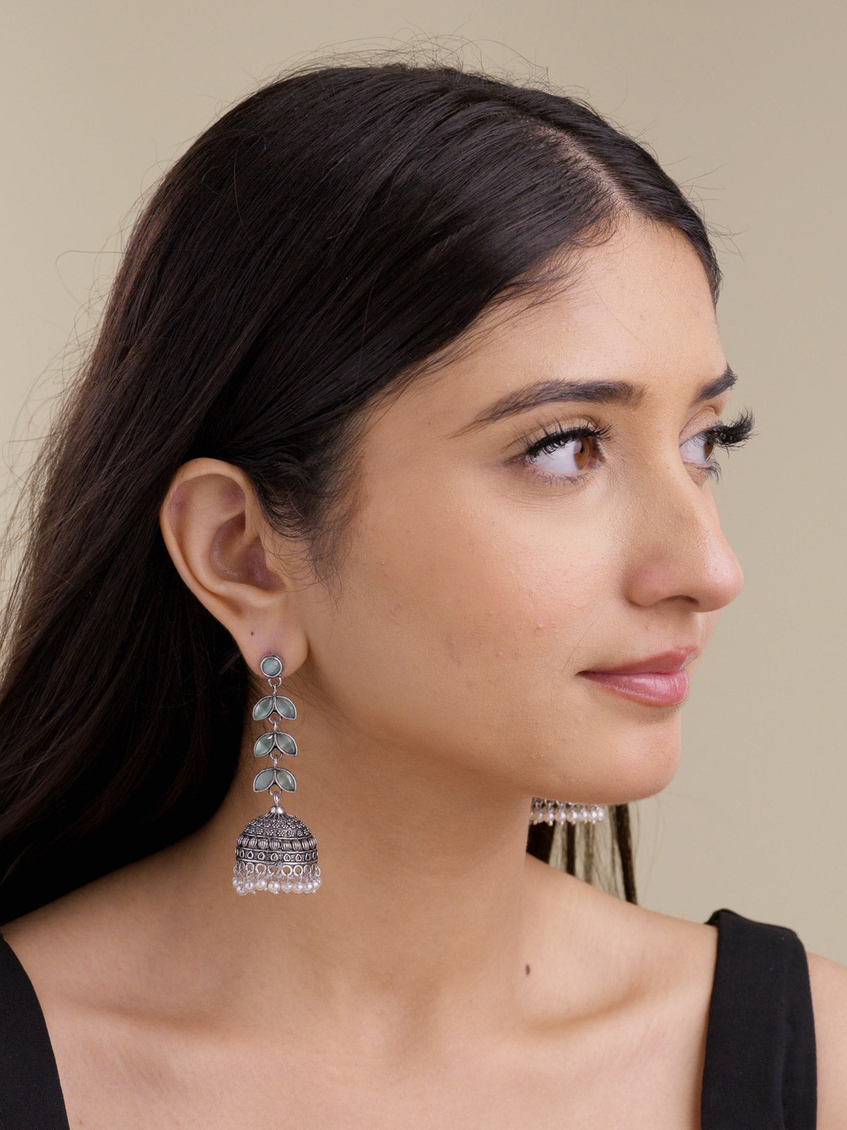 Model wearing oxidised jhumka earrings with a round mint stud, mint petal-shaped stones, textured dome detail, and pearl drops in a portrait shot.