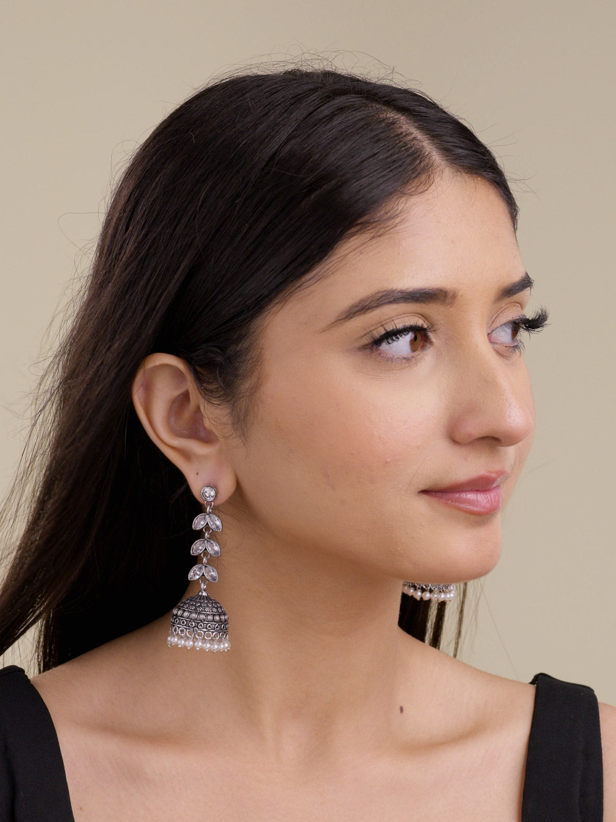 Model wearing oxidised jhumka earrings with clear petal-shaped stones, textured dome detail, and pearl drops in a portrait shot.