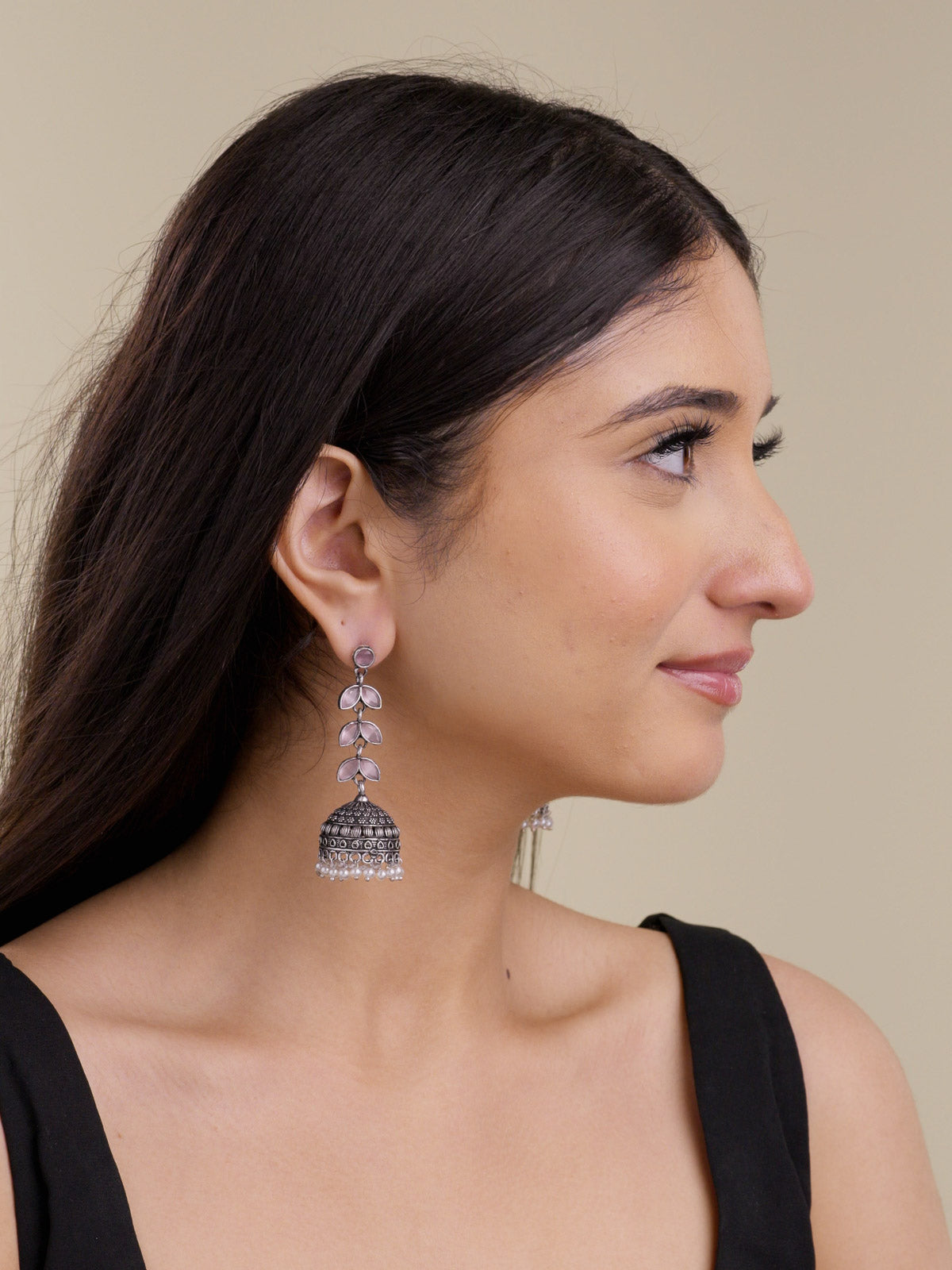 Model wearing oxidised jhumka earrings with pink petal-shaped stones, textured dome detail, and pearl drops in a side portrait shot.