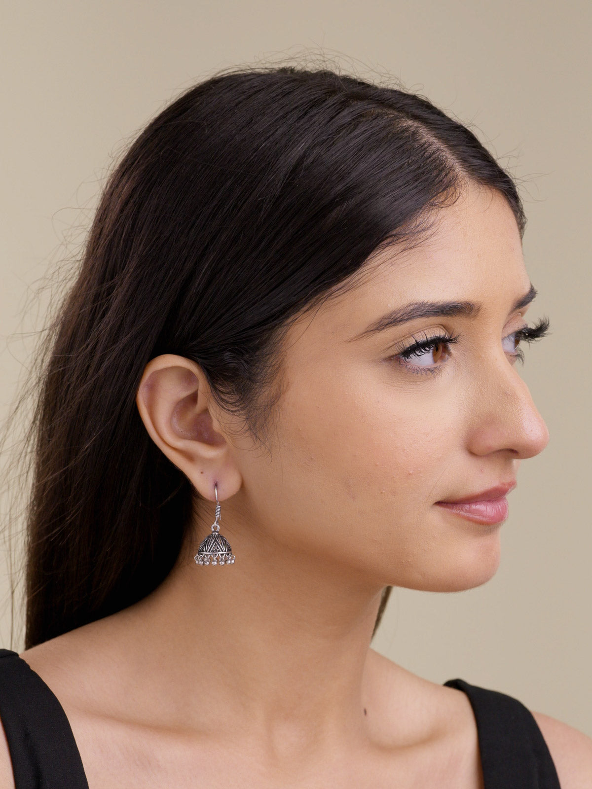 Portrait view of a model wearing a small oxidised jhumki earring with a patterned dome, hook-style top, and tiny metal drops along the lower edge.