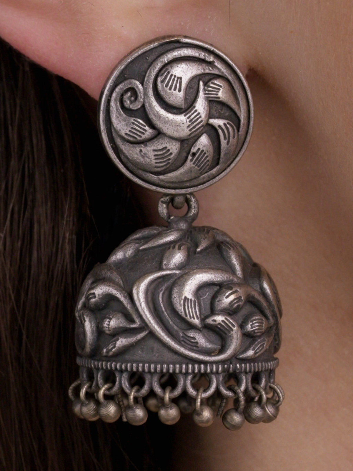 Oxidised jhumka earring with round carved stud, raised dome detailing and lower metal drops, close-up model-worn view.