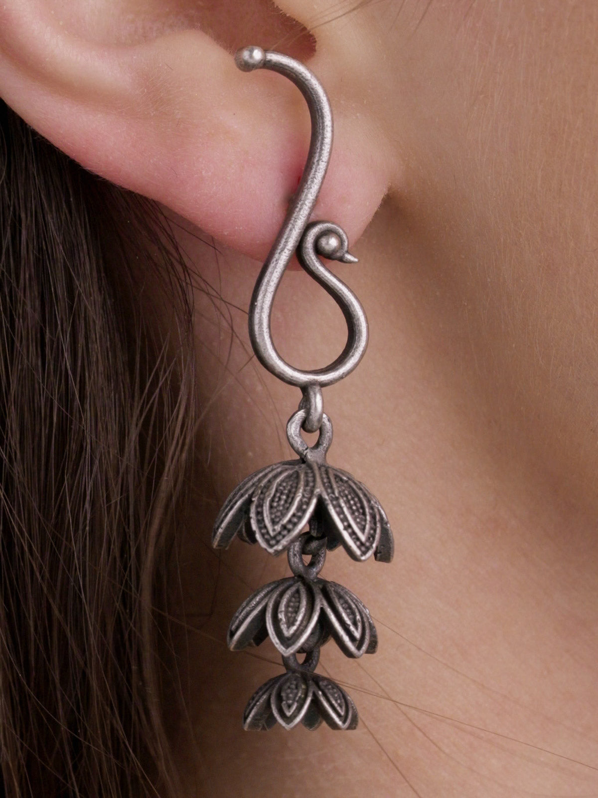 Close-up detail of neutral oxidised earrings with a peacock-inspired curved top and three-tier leaf-shaped jhumki-style drop.