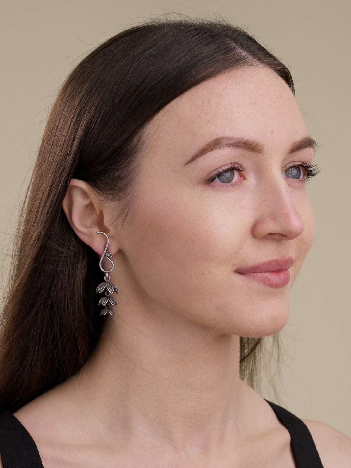 Model wearing neutral oxidised earrings with a peacock-inspired curved top and three-tier leaf-shaped jhumki-style drop.