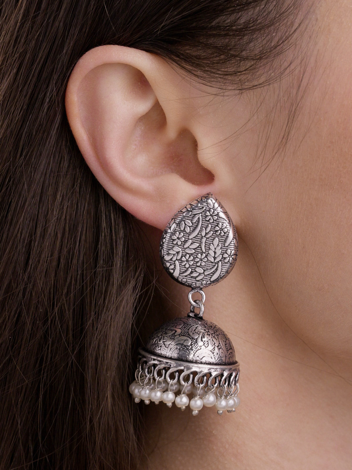 Model wearing silver-look oxidised jhumka earrings with floral and leaf-pattern stud top, carved dome, looped rim and pearl drops.