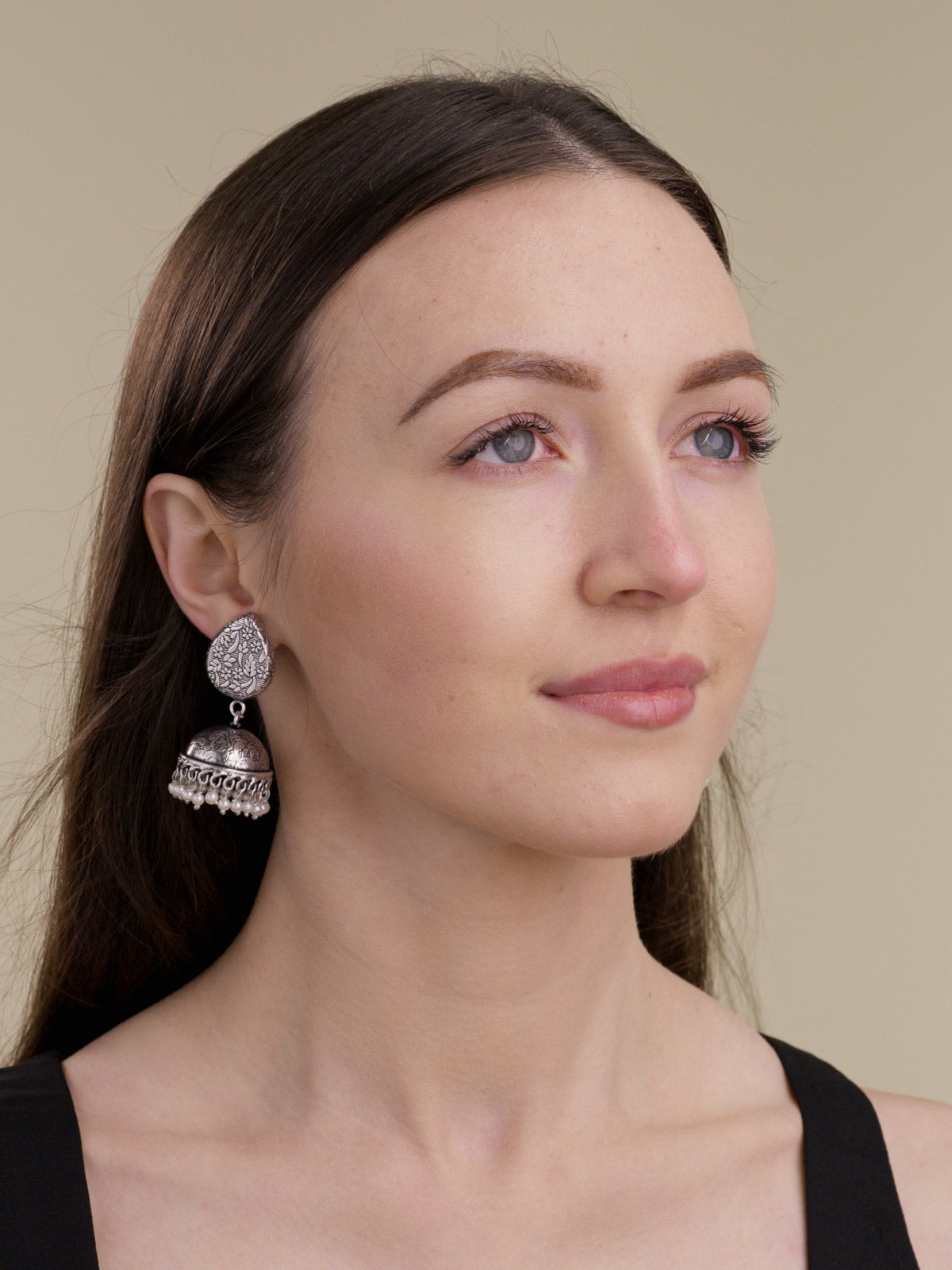 Model wearing silver-look oxidised jhumka earrings with floral and leaf-pattern stud top, carved dome detail, looped rim and pearl drops.