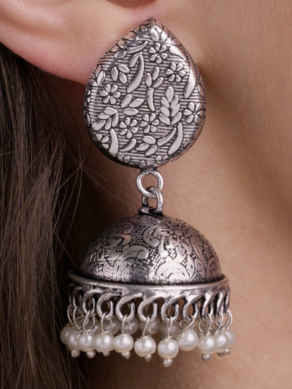 Close-up of silver-look oxidised jhumka earring with floral and leaf-pattern stud top, carved dome, looped rim and pearl drops.