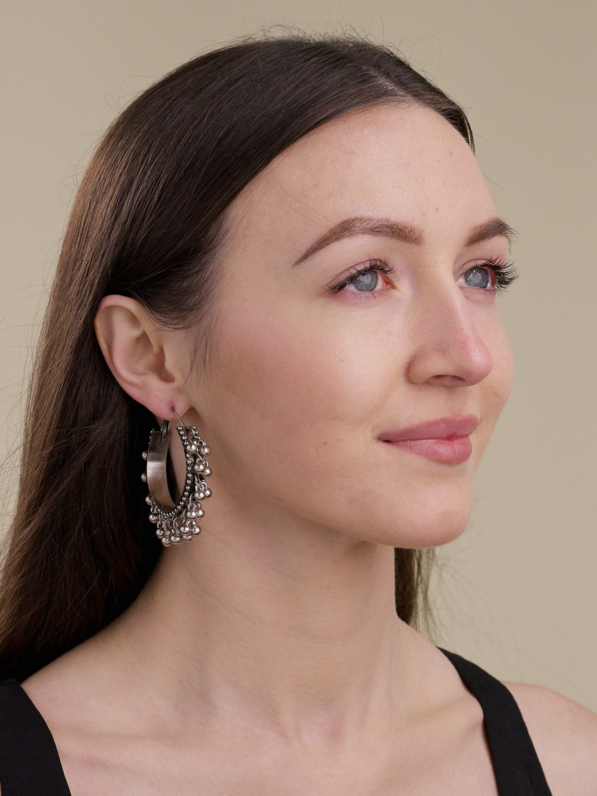 Model wearing oxidised bali hoop earrings with broad curved hoops, raised dot edging and small rounded metal drops in a side-facing portrait view.