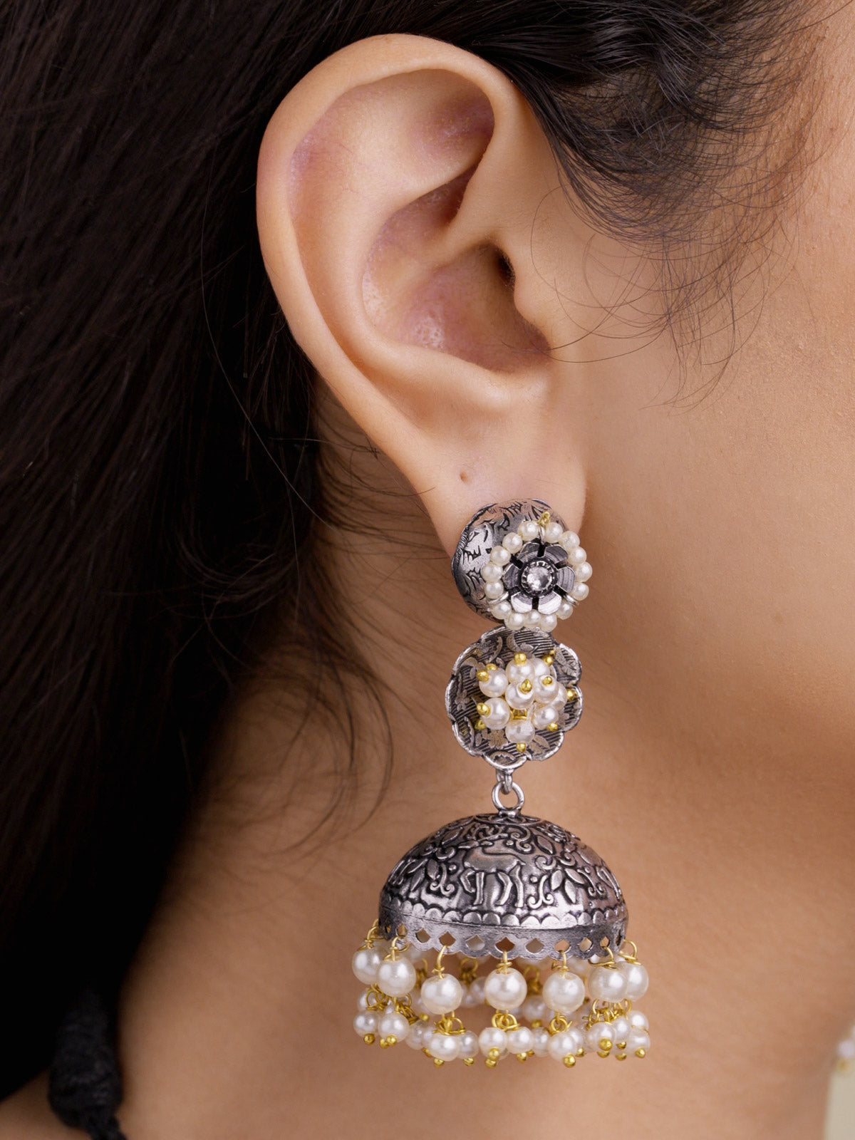 Close-up side view of a model wearing an oxidised jhumka earring with round floral medallion sections, a carved dome, pearl drops, subtle gold-tone accents, and a partially visible matching necklace.