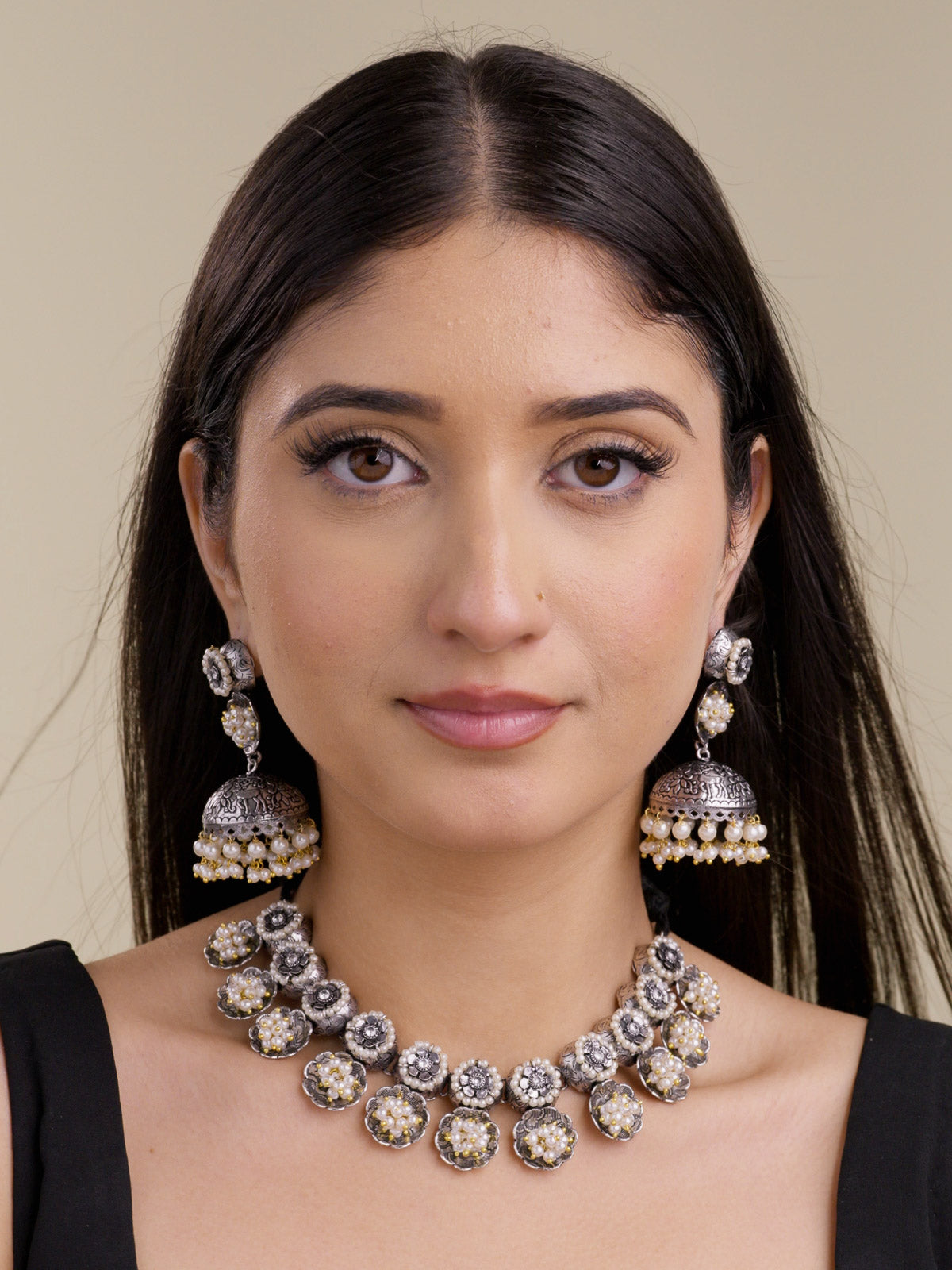 Model wearing an oxidised necklace set with round floral medallion links, pearl cluster drops, subtle gold-tone accents, and matching jhumka earrings in a front portrait shot.