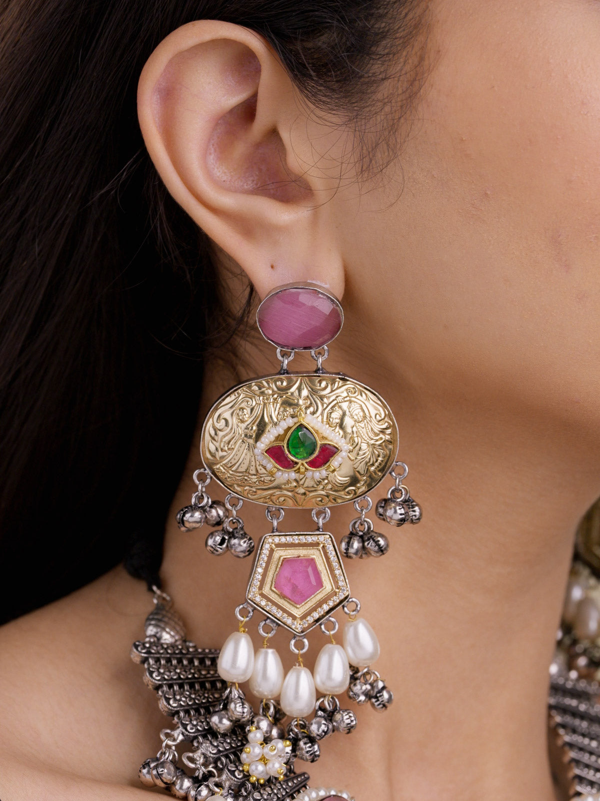 Close-up side view of a model wearing a statement multi tone oxidised earring with an antique gold oval medallion, pink stone top, small green and ruby red accents, pearl drops, metal bead drops, and part of the matching necklace partially visible below.