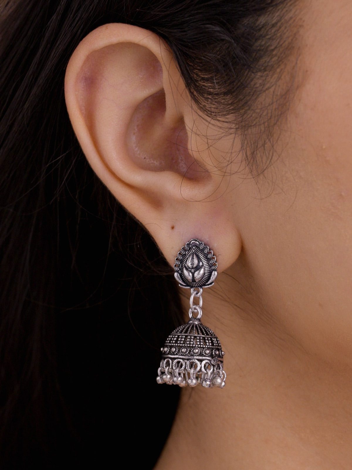 Close-up side view of a model wearing a small oxidised jhumki earring with a raised petal stud, linked connector, textured dome, and small rounded metal drops.