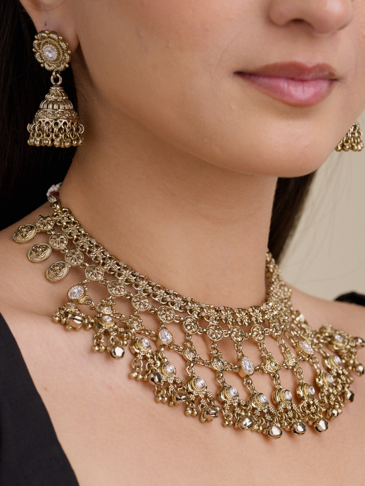 Rajwadi necklace set in antique gold tone with layered coin-style detailing, clear stone accents, hanging bead accents, and matching jhumka earrings shown close up.