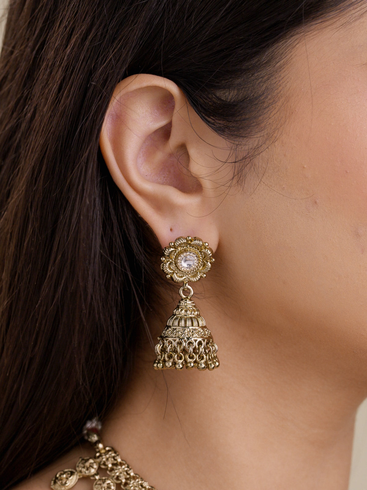 Rajwadi jhumka earring in antique gold tone with floral stud, clear centre stone, dome detail, and small hanging bead accents shown close up.