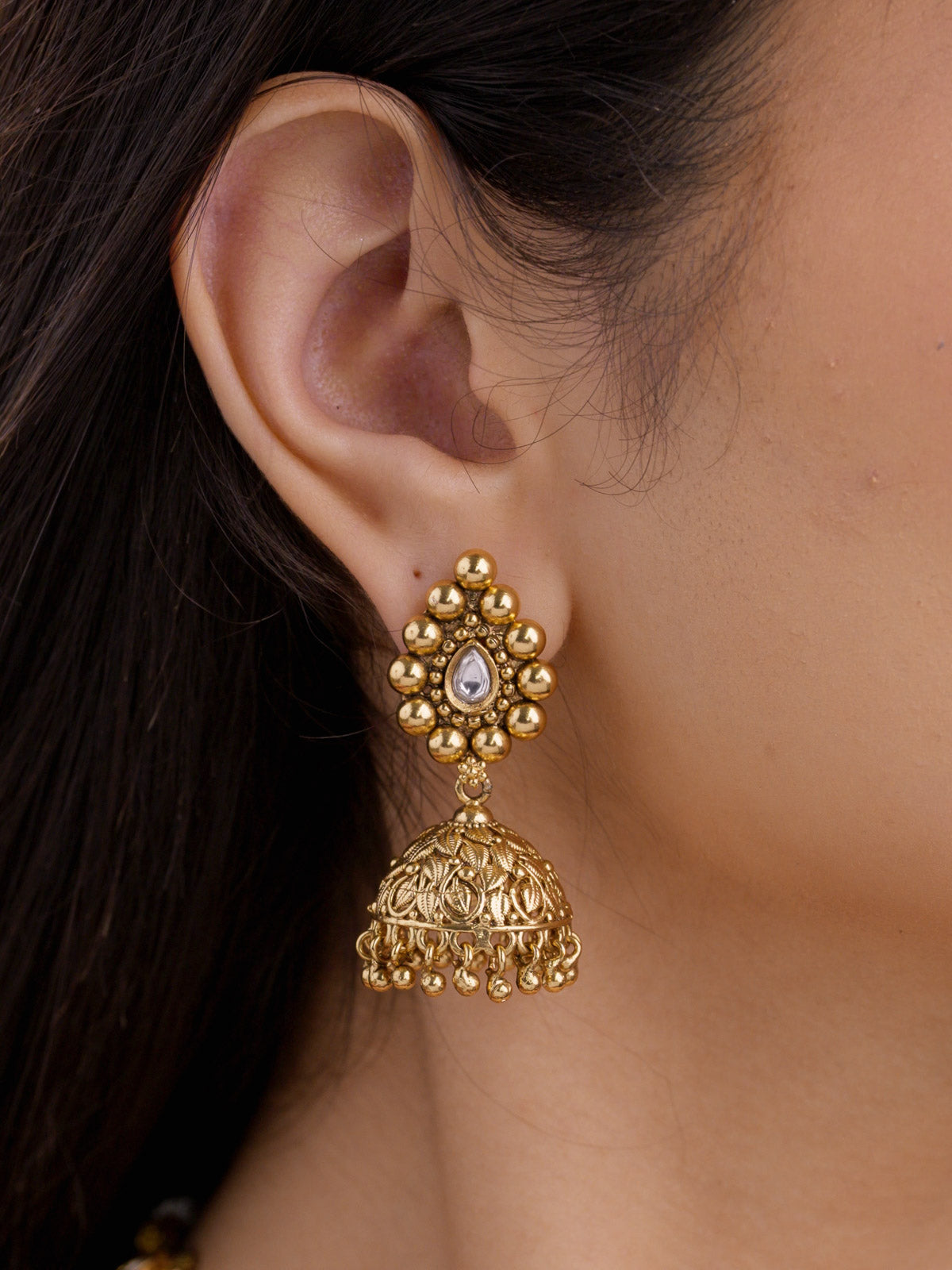 Close-up of a model wearing a gold tone Rajwadi jhumka earring with a teardrop stone centre, rounded bead detailing, and a carved dome drop.