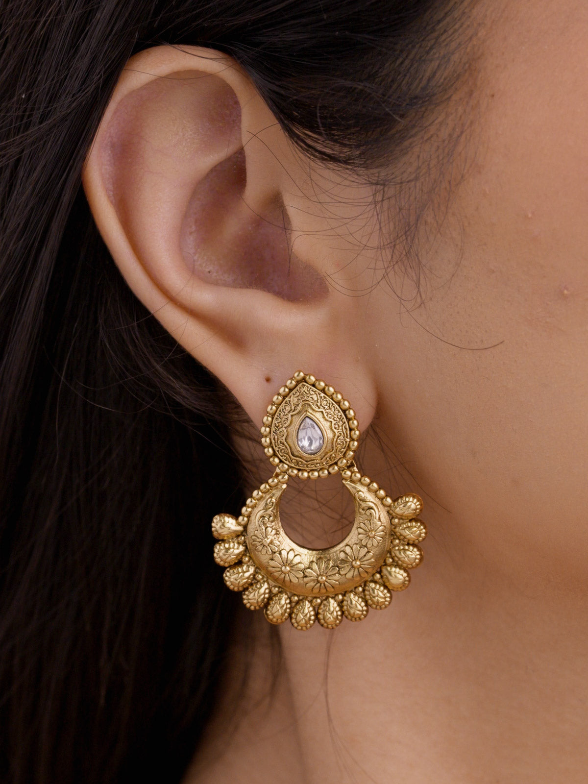 Close-up of a matching Rajwadi earring in matte gold tone, showing a teardrop white stone accent, open crescent shape, floral detailing, and small rounded edge drops.