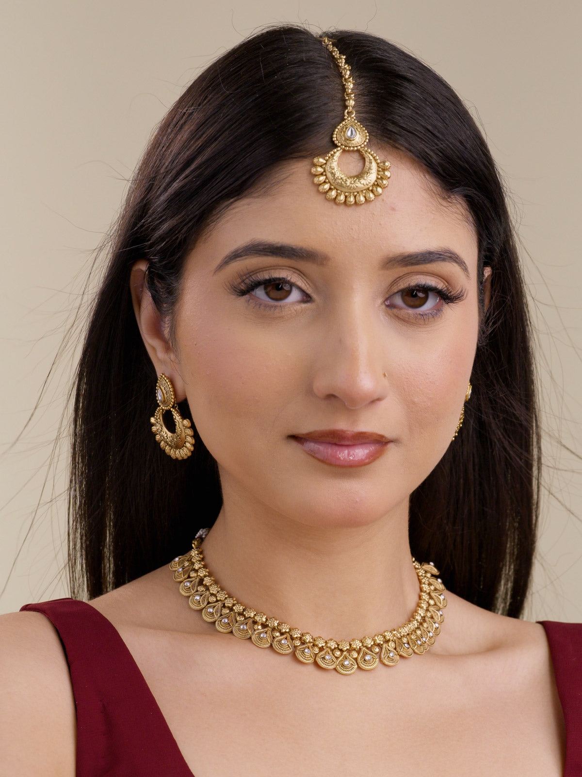 Model wearing a Rajwadi necklace set in matte gold tone with matching crescent earrings and maang tikka, showing repeated teardrop necklace detailing, white stone accents, and a close traditional set styling.