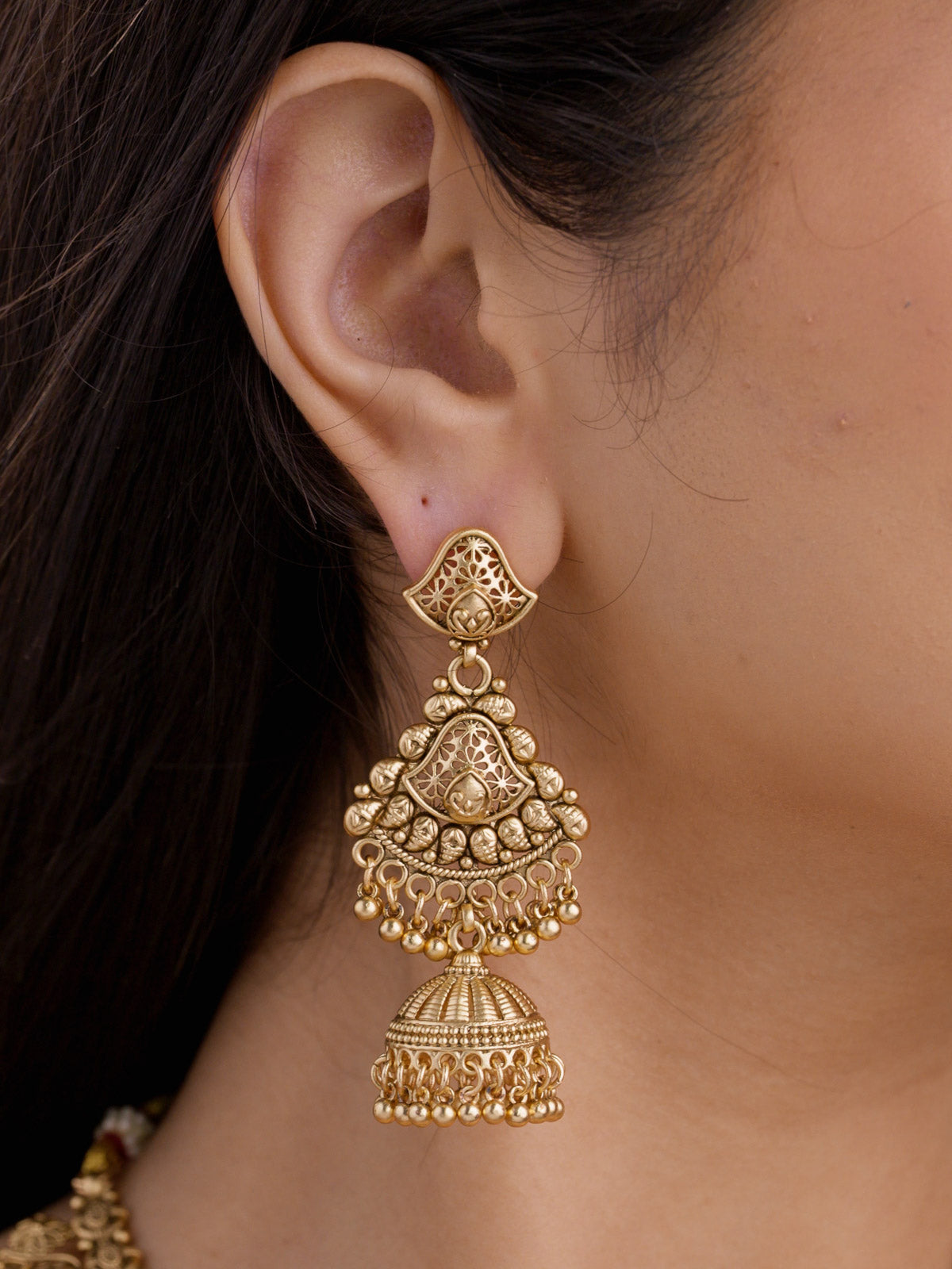 Close-up of model wearing a long matte gold tone Rajwadi jhumka earring with filigree-style openwork detailing, small rounded metal drops.