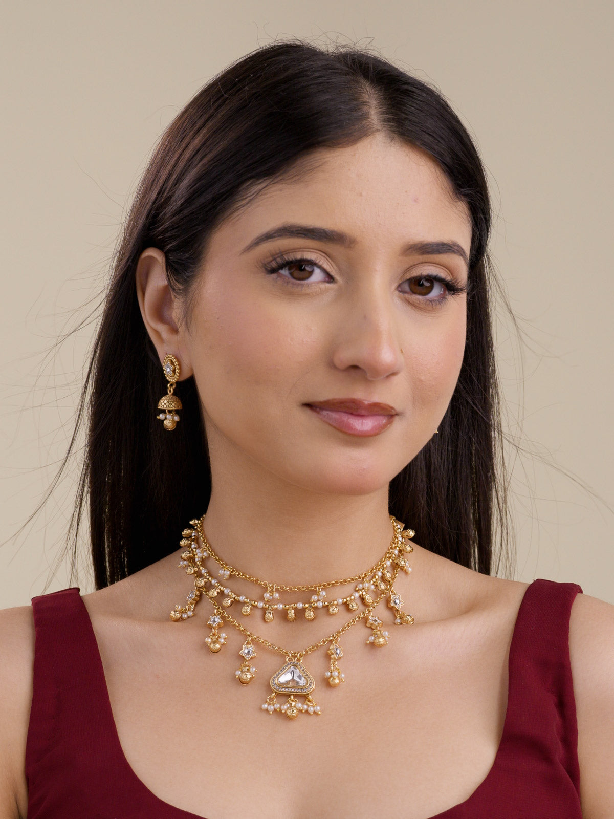 Model wearing a matte gold tone Rajwadi necklace set with layered chains, pearl-style drops, a centre white accent stone, and matching small jhumka earrings.