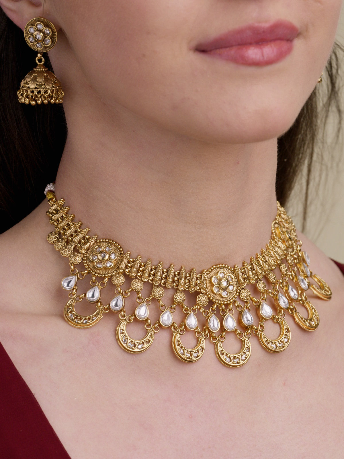 Rajwadi necklace set in matte gold tone with floral medallion details, clear teardrop stones, half-moon lower charms, and matching jhumka earring on model close-up