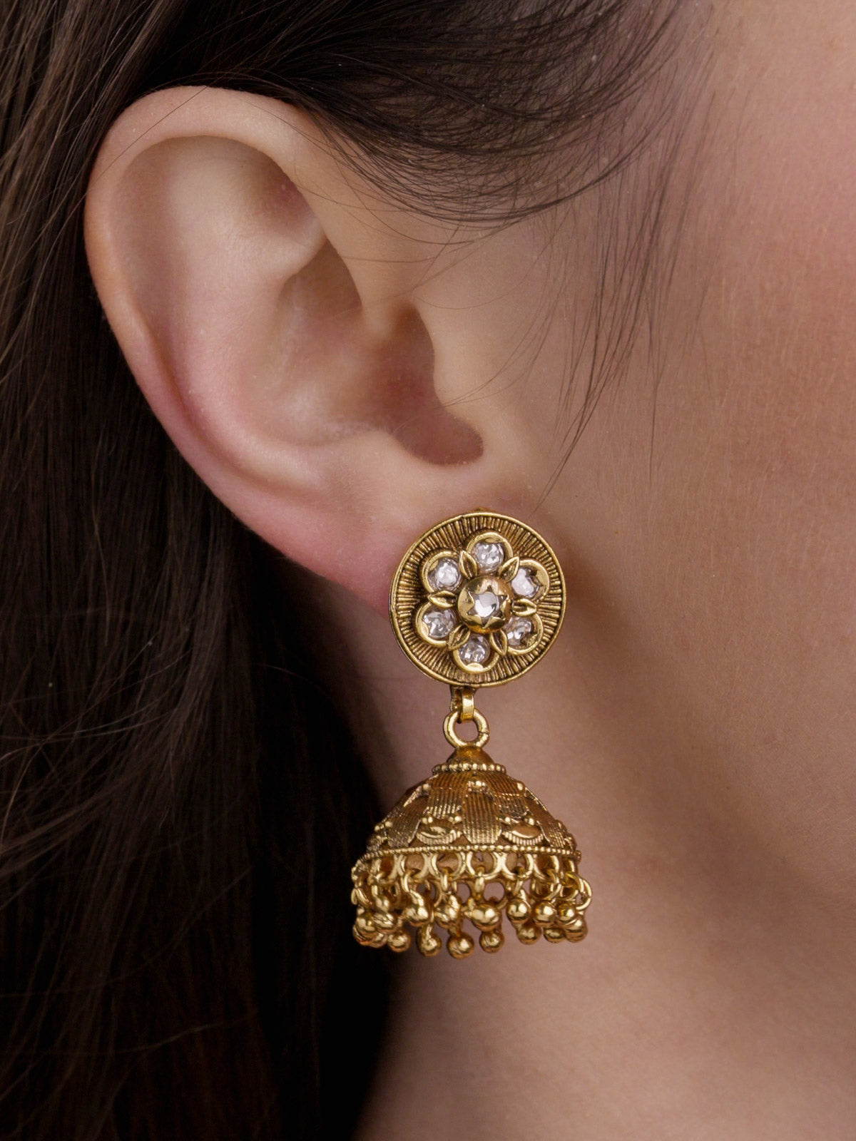 Rajwadi jhumka earring in matte gold tone with floral stud top, clear stone details, dome drop, and small round metal drops on model detailed close-up